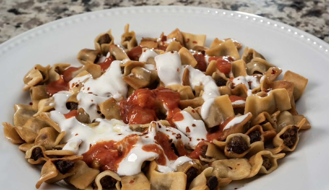 Close-up of manti with yogurt, tomato sauce and chili flakes