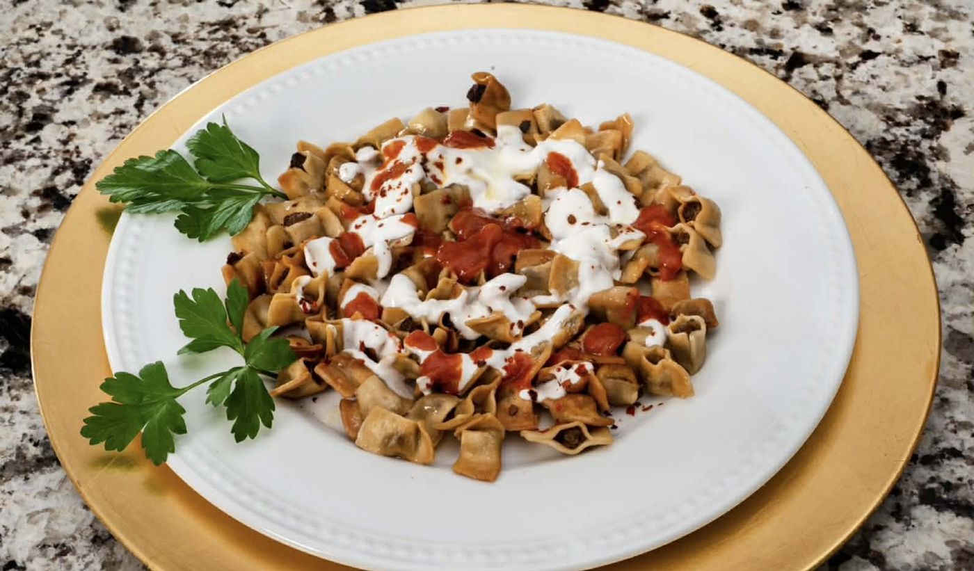 Manti served on a white plate over a gold charger