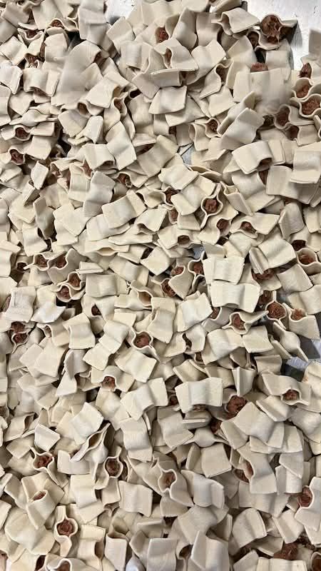 Hundreds of uncooked manti dumplings, each a small open square of dough pinched around beef